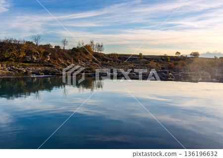 Tranquil Lake Shore With Rocky Banks, Autumn Trees, And Calm Reflections Under a Clear Sky Tranquil Lake Shore With Rocky Banks, Autumn Trees, And Calm Reflections Under a Clear Sky 136196632