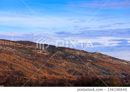 Autumn Hillside With Wind Turbines Under Blue Sky Over Colorful Foliage Landscape 136196648