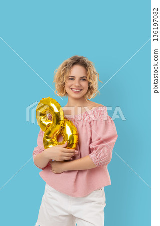 Woman smiles while holding gold balloons in the shape of eight Woman smiles while holding gold balloons in the shape of eight 136197082