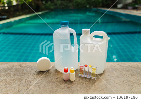 Pool maintenance chemicals and water testing kit with chlorine tablet and plastic containers on pool edge, clean swimming pool background Pool maintenance chemicals and water testing kit with chlorine tablet and plastic containers on pool edge, clean swimming pool background 136197186