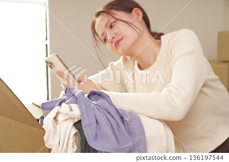 一位女士一邊使用智慧型手機一邊整理雜物。 136197544
