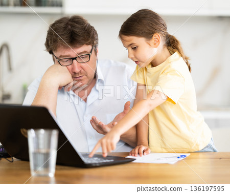 Father helps daughter do homework using laptop 136197595