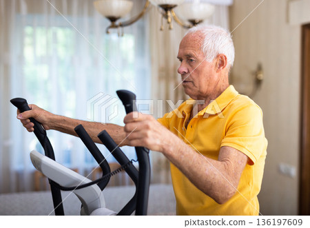 Elderly man exercising on elliptic trainer in living room 136197609