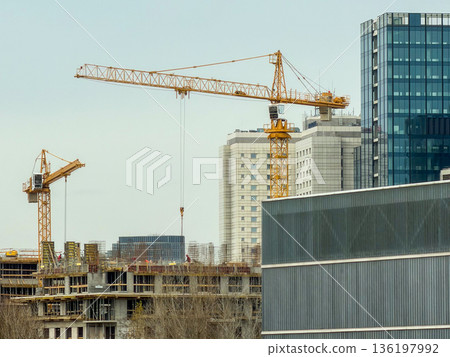 Large yellow construction cranes actively engaged on a sprawling building site in a modern city, symbolizing urban development and infrastructure growth Large yellow construction cranes actively engaged on a sprawling building site in a modern city, symbolizing urban development and infrastructure growth 136197992