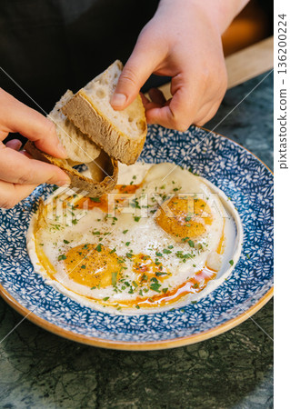 Hands dipping sourdough bread into traditional turkish eggs 136200224