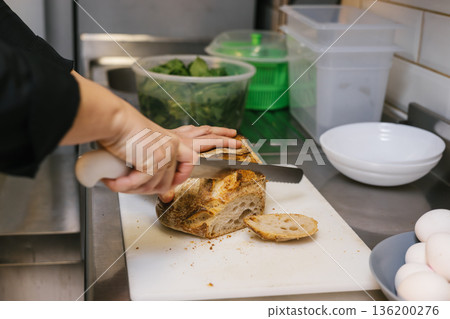 Baker cutting fresh artisanal sourdough bread in kitchen 136200276