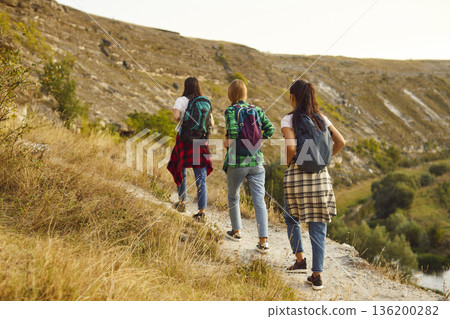 Group of young girls tourists with backpacks hiking in nature walking in a row. 136200282