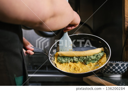 Chef preparing omelet with spinach and cheese filling 136200284