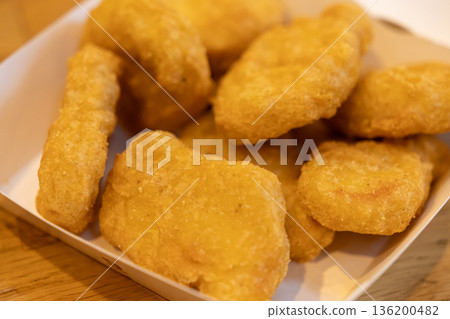 Crispy golden fried chicken nuggets in a white paper container, representing a classic quick service restaurant appetizer, convenient snack, or satisfying takeaway meal Crispy golden fried chicken nuggets in a white paper container, representing a classic quick service restaurant appetizer, convenient snack, or satisfying takeaway meal 136200482