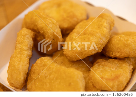Crispy golden brown fried chicken nuggets served in a white cardboard container, ideal for a quick delicious fast food snack or a satisfying takeaway meal 136200486