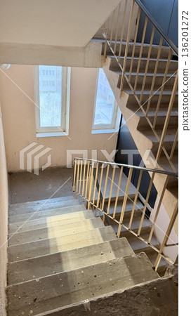 Residential apartment building stairwell with concrete stairs, metal railings and windows, empty interior with natural daylight. Residential apartment building stairwell with concrete stairs, metal railings and windows, empty interior with natural daylight. 136201272