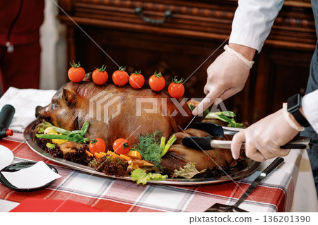 Roast pig with vegetables, gloved chef's hands cut with a knife Roast pig with vegetables, gloved chef's hands cut with a knife 136201390
