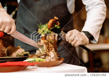 Roast pig with vegetables, gloved chef's hands cut with a knife Roast pig with vegetables, gloved chef's hands cut with a knife 136201392