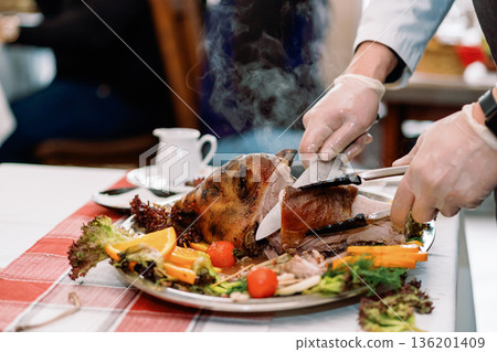 Roast pig with vegetables, gloved chef's hands cut with a knife 136201409