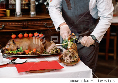 Roast pig with vegetables, gloved chef's hands cut with a knife Roast pig with vegetables, gloved chef's hands cut with a knife 136201410