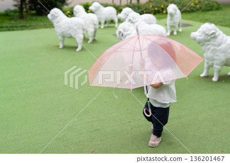 一個嬰兒撐著傘在公園的草地上行走。 一個嬰兒撐著傘在公園的草地上行走。 136201467