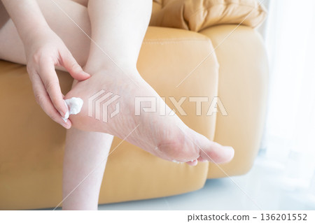 Woman applying cream for treatment peeling and cracked foot. Causes of peeling foot included fungal infection (athlete's foot), dermatitis (eczema), sunburn, dry skin, dehydration or sweaty feet. 136201552