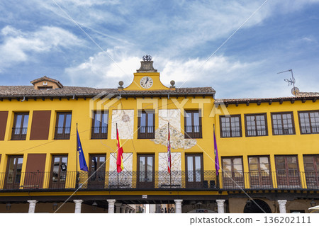 Historic yellow building facade with flags and a clock under blue sky 136202111