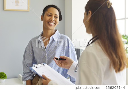 Experienced woman doctor giving consultation during medical consultation, writing down notes  136202144
