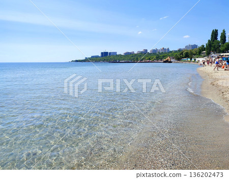 Beautiful blue sea with sandy beach and blue sky, lots of people on beach and city on hills with green trees on sunny hot summer day. Coastline on sea. Seascape. Vacation tourism travel rest 136202473