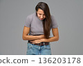 Woman holding stomach and bending forward in discomfort, studio image on grey 136203178