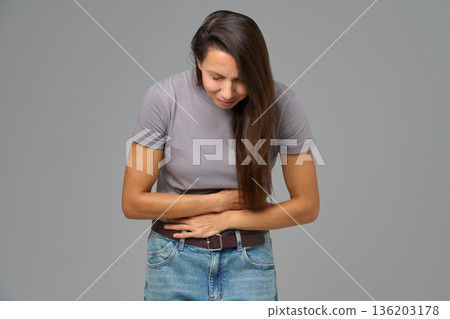 Woman holding stomach and bending forward in discomfort, studio image on grey 136203178