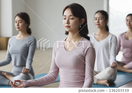 Group of women are sitting on yoga mats and meditating 136203539