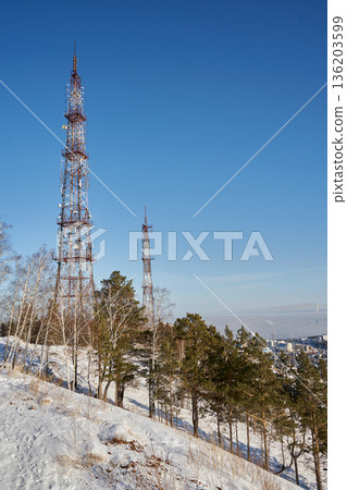 Two telecommunication towers on a snowy hill, modern communication infrastructure with pine trees and birch trees in winter. Two telecommunication towers on a snowy hill, modern communication infrastructure with pine trees and birch trees in winter. 136203599