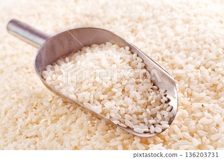 Raw rice spill out of a metal scoop on a light table 136203731