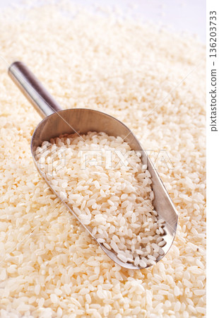 Raw rice spill out of a metal scoop on a light table 136203733