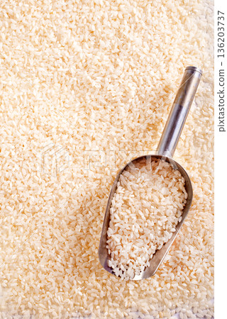 Raw rice spill out of a metal scoop on a light table 136203737