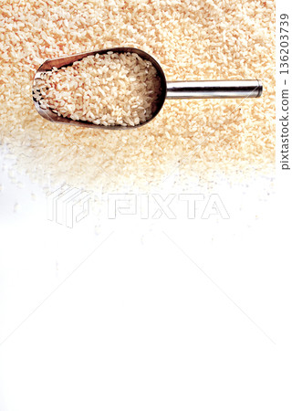 Raw rice spill out of a metal scoop on a light table 136203739