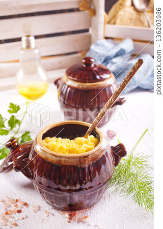 Corn porridge in a clay plate, a clay pot with porridge on a light background Corn porridge in a clay plate, a clay pot with porridge on a light background 136203986