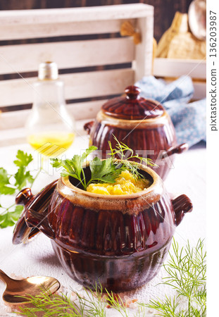 Corn porridge in a clay plate, a clay pot with porridge on a light background 136203987