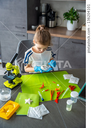 Young girl holding crescent shaped crystal grown at home and carefully examining its surface and structure. Creative STEM experiment combining science learning with artistic crystal growing project. Young girl holding crescent shaped crystal grown at home and carefully examining its surface and structure. Creative STEM experiment combining science learning with artistic crystal growing project. 136204101