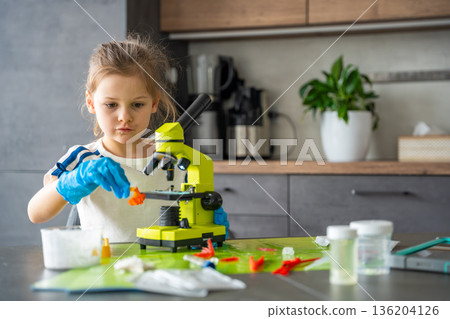 Young girl holding grown crystal and preparing it for detailed examination under microscope during home science experiment. STEM education and practical learning through crystal growing activity Young girl holding grown crystal and preparing it for detailed examination under microscope during home science experiment. STEM education and practical learning through crystal growing activity 136204126