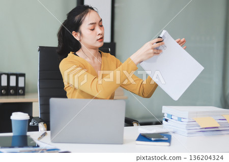 Young professional woman suffering from headache while analyzing financial charts and graphs on computer, experiencing work related stress in modern office Young professional woman suffering from headache while analyzing financial charts and graphs on computer, experiencing work related stress in modern office 136204324