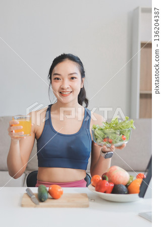 Fit young Asian women in activewear sitting on yoga mat and eating fresh vegetable salad after workout, representing clean eating, fitness lifestyle, wellness routine and health balance. 136204387