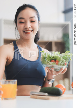 Fit young Asian women in activewear sitting on yoga mat and eating fresh vegetable salad after workout, representing clean eating, fitness lifestyle, wellness routine and health balance. 136204394