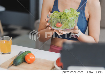 Fit young Asian women in activewear sitting on yoga mat and eating fresh vegetable salad after workout, representing clean eating, fitness lifestyle, wellness routine and health balance. Fit young Asian women in activewear sitting on yoga mat and eating fresh vegetable salad after workout, representing clean eating, fitness lifestyle, wellness routine and health balance. 136204396