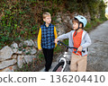 Two young boys walking with a bicycle outdoors and talking, childhood friendship and active lifestyle 136204410