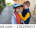 One boy helping another fasten a bicycle helmet outdoors, care, safety and childhood friendship. 136204413