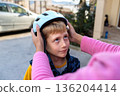 Adult hands adjusting a bicycle helmet on a young boy outdoors, child safety, care and protection before cycling 136204414