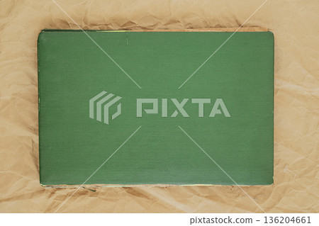 Vintage green book cover lying on crumpled craft paper background. Concept of retro book mockup with empty surface for text or design 136204661