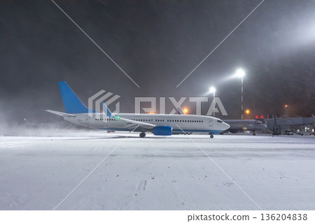 Taxiing of a passenger airplane at the airport in a snow blizzard at night 136204838