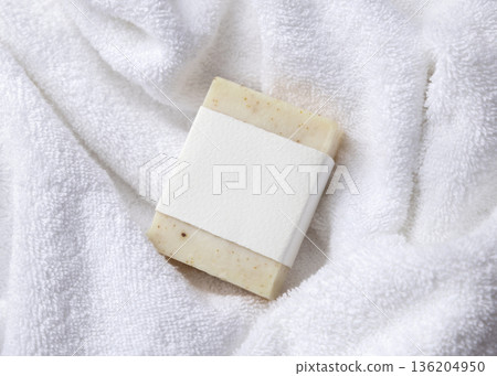 Mockup of beige solid soap bar with blank paper label on white bath towel, personal care packaging 136204950