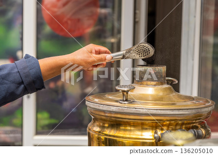 Adult person interacting with metal hot water urn outdoors Adult person interacting with metal hot water urn outdoors 136205010