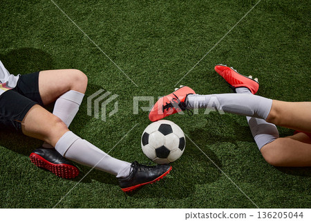 Female soccer players foot duel for ball on artificial turf. 136205044
