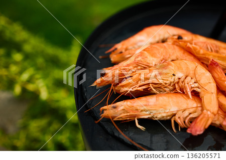 Grilled shrimp on a black grill plate surrounded by green grass in a sunny outdoor setting Grilled shrimp on a black grill plate surrounded by green grass in a sunny outdoor setting 136205571