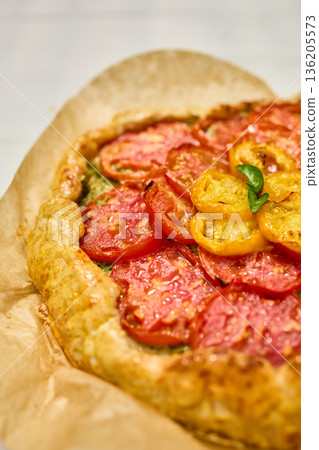 Freshly baked tomato galette on parchment paper served on a rustic wooden table in a cozy kitchen setting Freshly baked tomato galette on parchment paper served on a rustic wooden table in a cozy kitchen setting 136205573